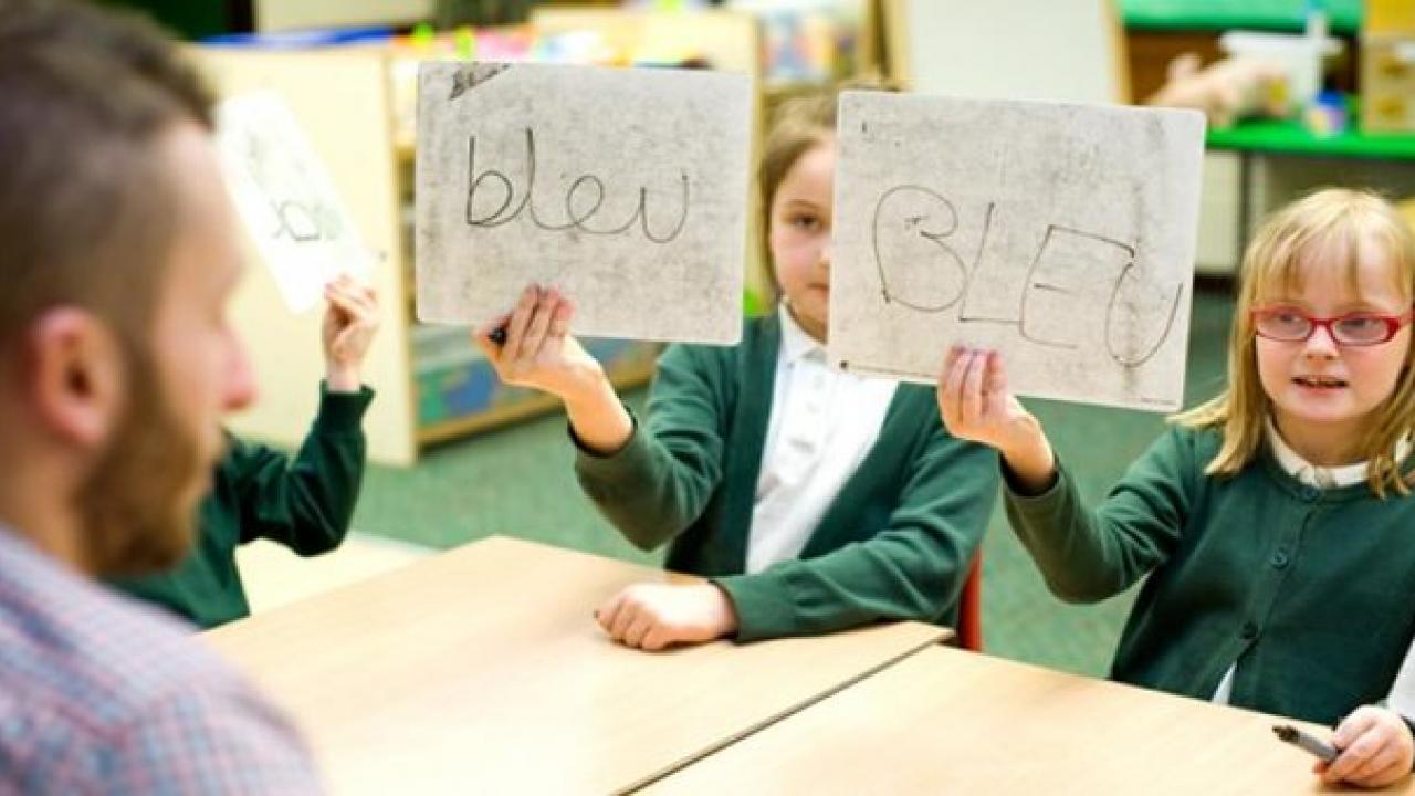 Image of a teacher and two children holding up whiteboards with the word 'BLEU' on.