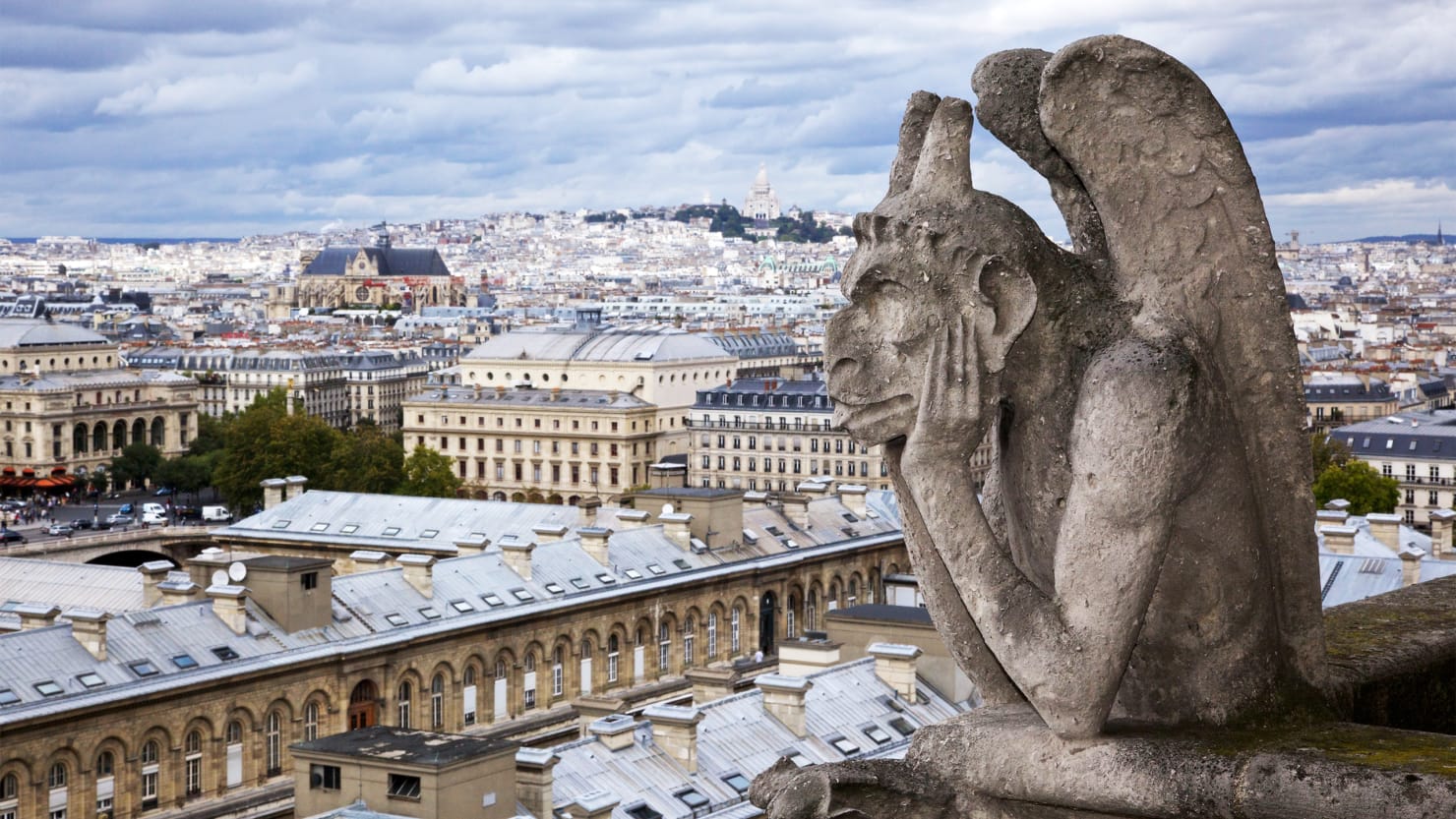 Blurred image of Paris, with the Gargoyle of Notre Dame with their head in their hands in the forefront, in focus.